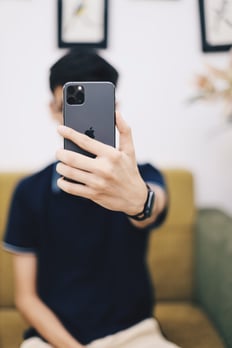 Ein Mann hält sich mit ausgestrecktem Arm ein Handy vor das Gesicht.